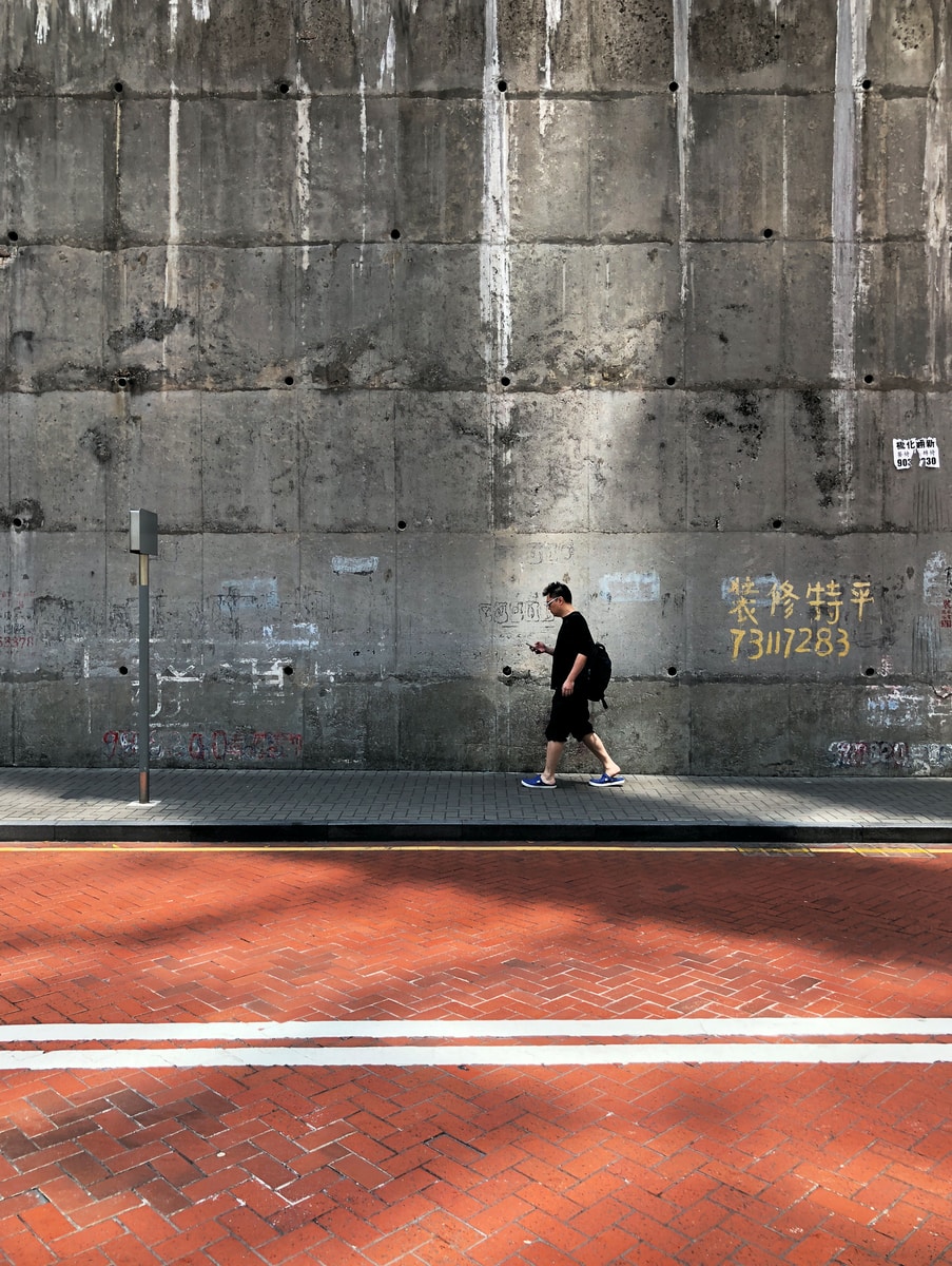 man walking beside wall and street during daytime
